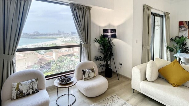 A modern living room with a large window, a white sofa, two armchairs, a small side table, and a floor lamp. - Lux 2 Bed l Stunning Sea View I Steps to JBR Beach I Sadaf 6 (Jumeirah Beach Residence)