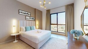 Een moderne hotelkamer met een groot bed, een klein nachtkastje, een bureau met spiegel en uitzicht op de stad door grote ramen.