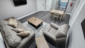 A modern living room with a gray sofa set, a coffee table, and a dining area with a wooden table and chairs. - Paradise on Lake Harris Apt #201 (Leesburg)