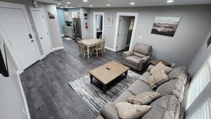 A modern living room with a sofa, armchair, coffee table, and dining area. - Paradise on Lake Harris Apt #201 (Leesburg)