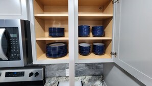A kitchen with white cabinets, a microwave, and a stove. There are shelves with blue bowls and plates. - Paradise on Lake Harris Apt #201 (Leesburg)