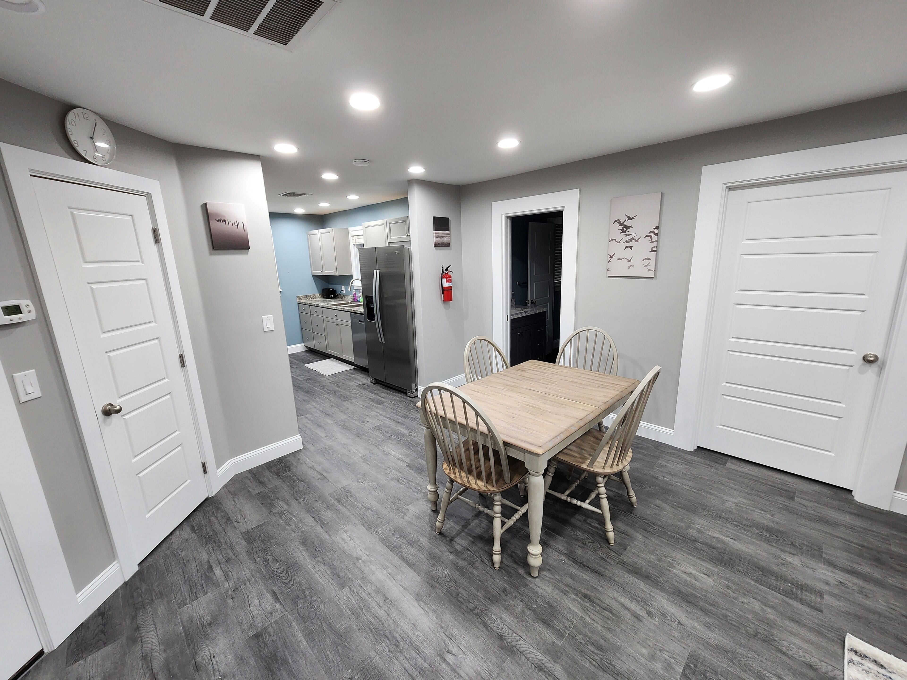A modern kitchen with stainless steel appliances, a dining area with a wooden table and chairs, and a hallway leading to other rooms.
