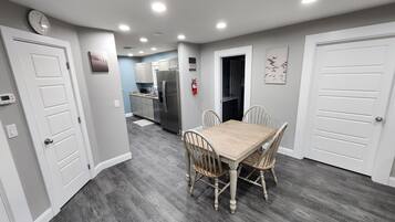 A modern kitchen with stainless steel appliances, a dining area with a wooden table and chairs, and a hallway leading to other rooms.