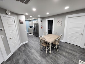 A modern kitchen with stainless steel appliances, a dining area with a wooden table and chairs, and a hallway leading to other rooms.