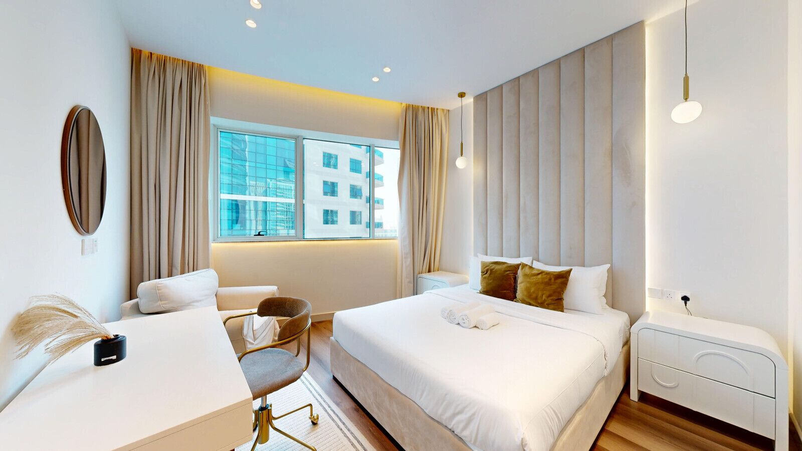 A modern hotel room with a large bed, a desk, a chair, and a nightstand.