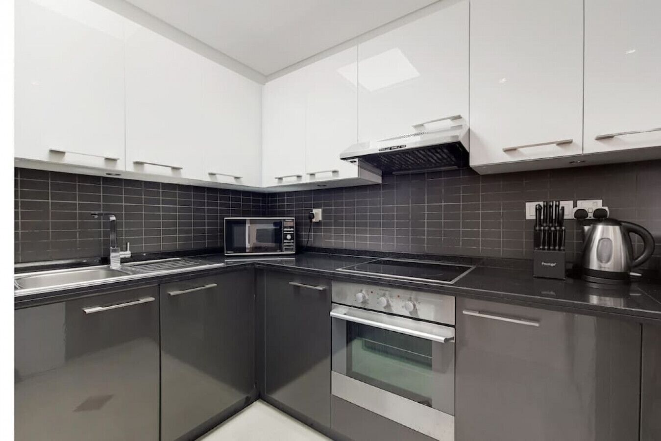 Une cuisine moderne avec des meubles de couleur gris foncé, un four à micro-ondes en acier inoxydable, une cuisinière à gaz et une bouilloire.