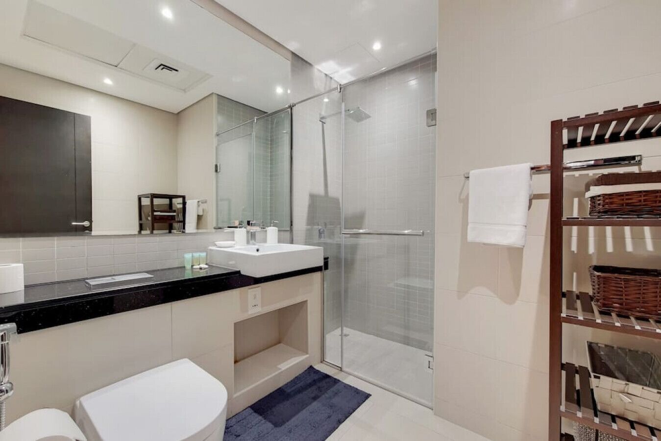 Une salle de bain moderne avec une douche à parois de verre, un lavabo blanc et une étagère intégrée avec des paniers.