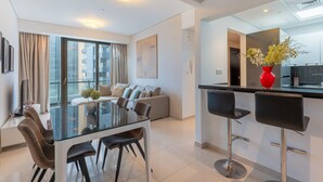 Een moderne woonkamer met een glazen eettafel, een bank en een keukenhoek met een rode vaas.