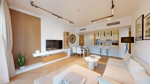 Een moderne woonkamer met een flatscreen televisie, een eethoek en een keuken op de achtergrond.