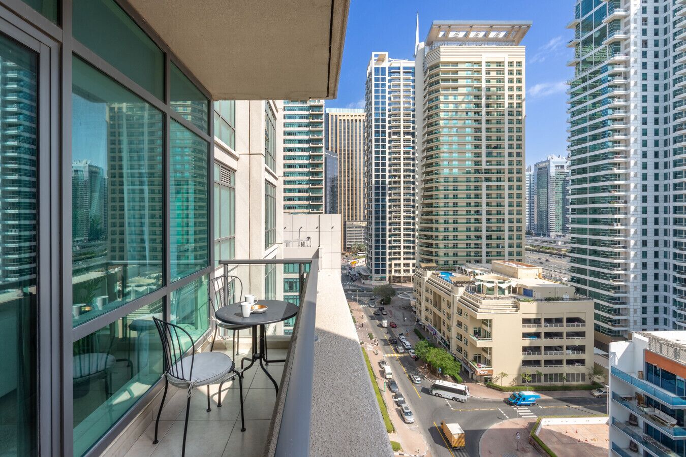 Un balcon avec une table et des chaises, donnant sur un paysage urbain avec de hauts immeubles.