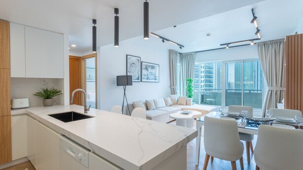 Een moderne keuken met een centraal eiland, een eethoek met een ronde tafel en een zithoek met een bank en een groot raam met uitzicht op de stad.