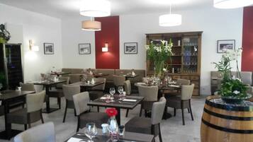 A restaurant with multiple tables and chairs, a bar area, and a bookshelf in the background.