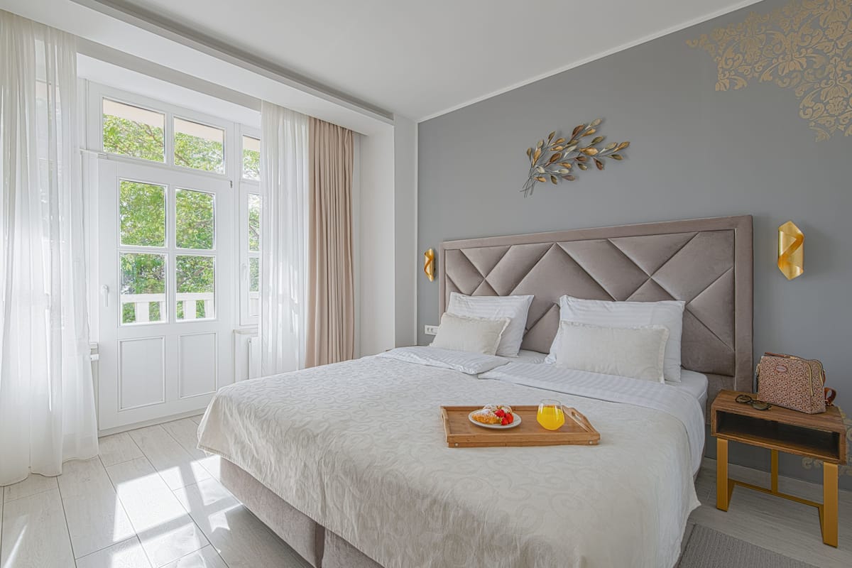 Un dormitori amb un llit gran, una tauleta de nit, una finestra amb cortines i una decoració mural.