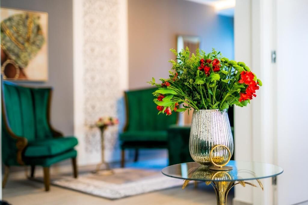 Et værelse med et glastæppe, der bærer en vase med røde blomster, grønne stole og et lille sofabord med en vase.