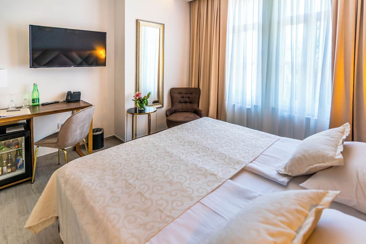 Una habitació d'hotel amb un llit, un escriptori amb un ordinador, una cadira, un televisor fixat a la paret i una finestra amb cortines.