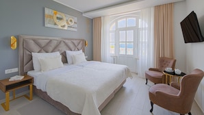 Une chambre d’hôtel dotée d’un grand lit, d’un coin salon avec un fauteuil et une table, d’une télévision et d’une fenêtre avec des rideaux.