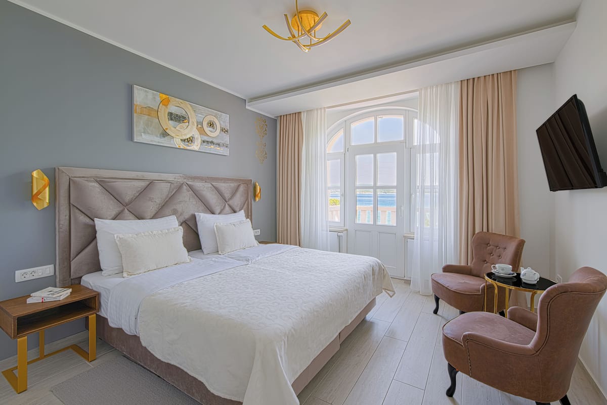 Una habitació d'hotel amb un llit gran, una zona de seients amb una cadira i taula, una televisió i una finestra amb cortines.