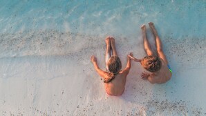 Deux personnes allongées sur une plage de sable fin, avec une eau cristalline.