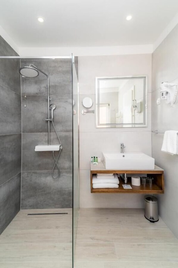 Een moderne badkamer met een douchecabine van glas, een houten wastafelmeubel met een witte wasbak en een grote spiegel erboven.