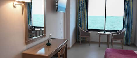 A hotel room with a bed, a desk, a chair, a TV, and a view of the sea.
