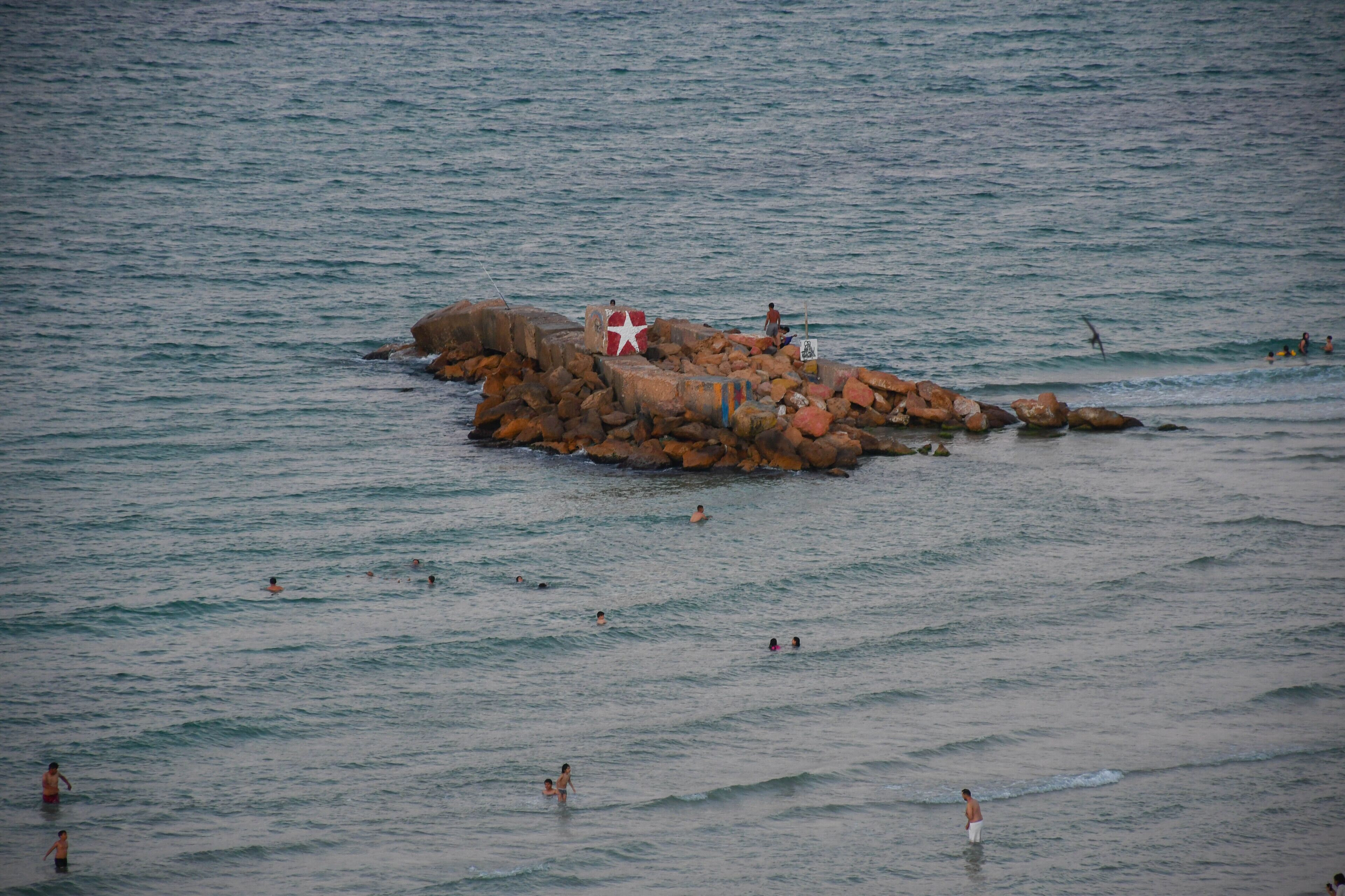 A rocky outcrop in the sea with people swimming around it.