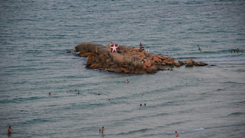 Ein felsiges Felsplateau im Meer, um das herum Menschen schwimmen.