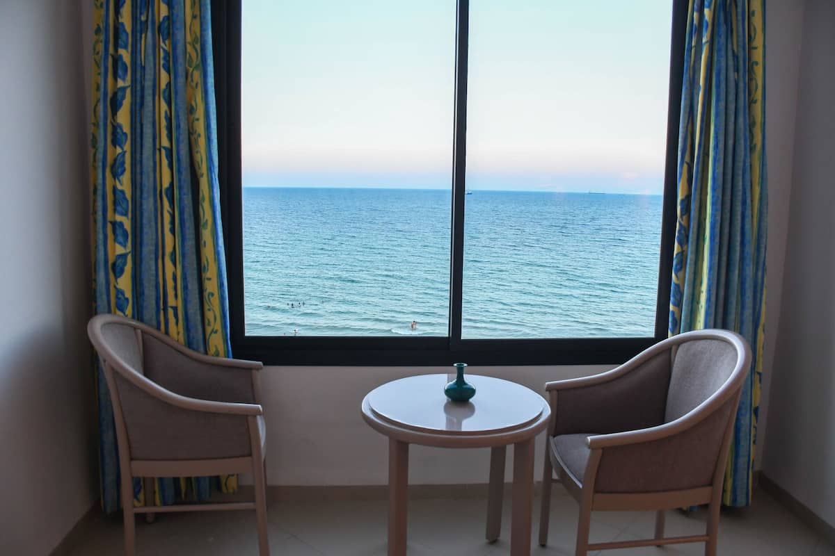 A room with a view of the sea, two chairs, and a small table.