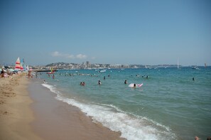 A beach with people swimming and sunbathing, boats in the water, and a cityscape in the background. - Studio and parking 300m from Fréjus beach (Fréjus)