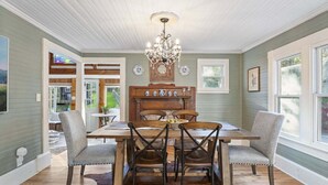 Un comedor con mesa y sillas de madera, una araña y vista al exterior.