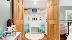Una habitación infantil con una muñeca, una mesita, dos sillas y cajas de almacenamiento.
