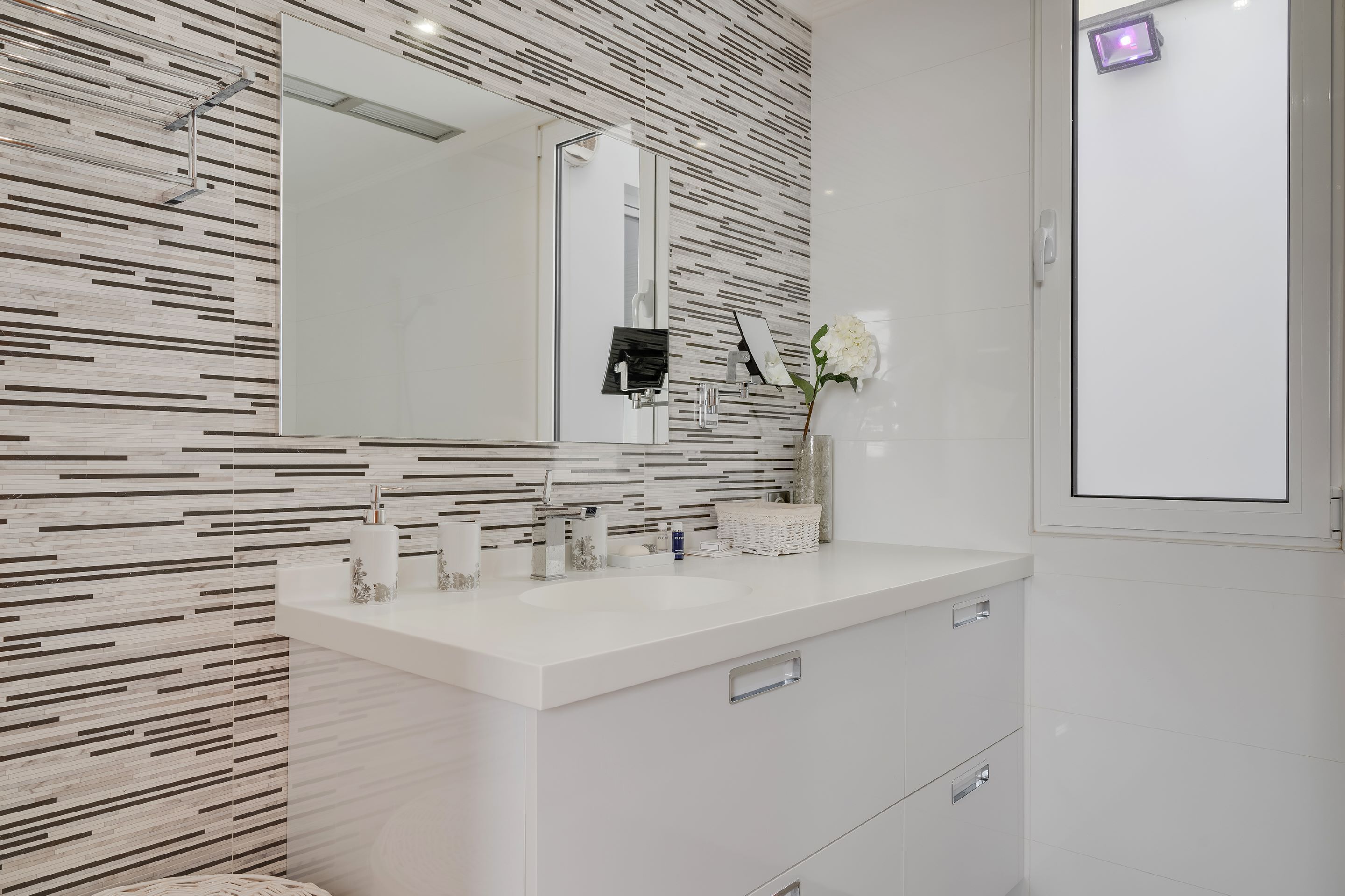 A modern bathroom with a white vanity, a large mirror, and a patterned wall.