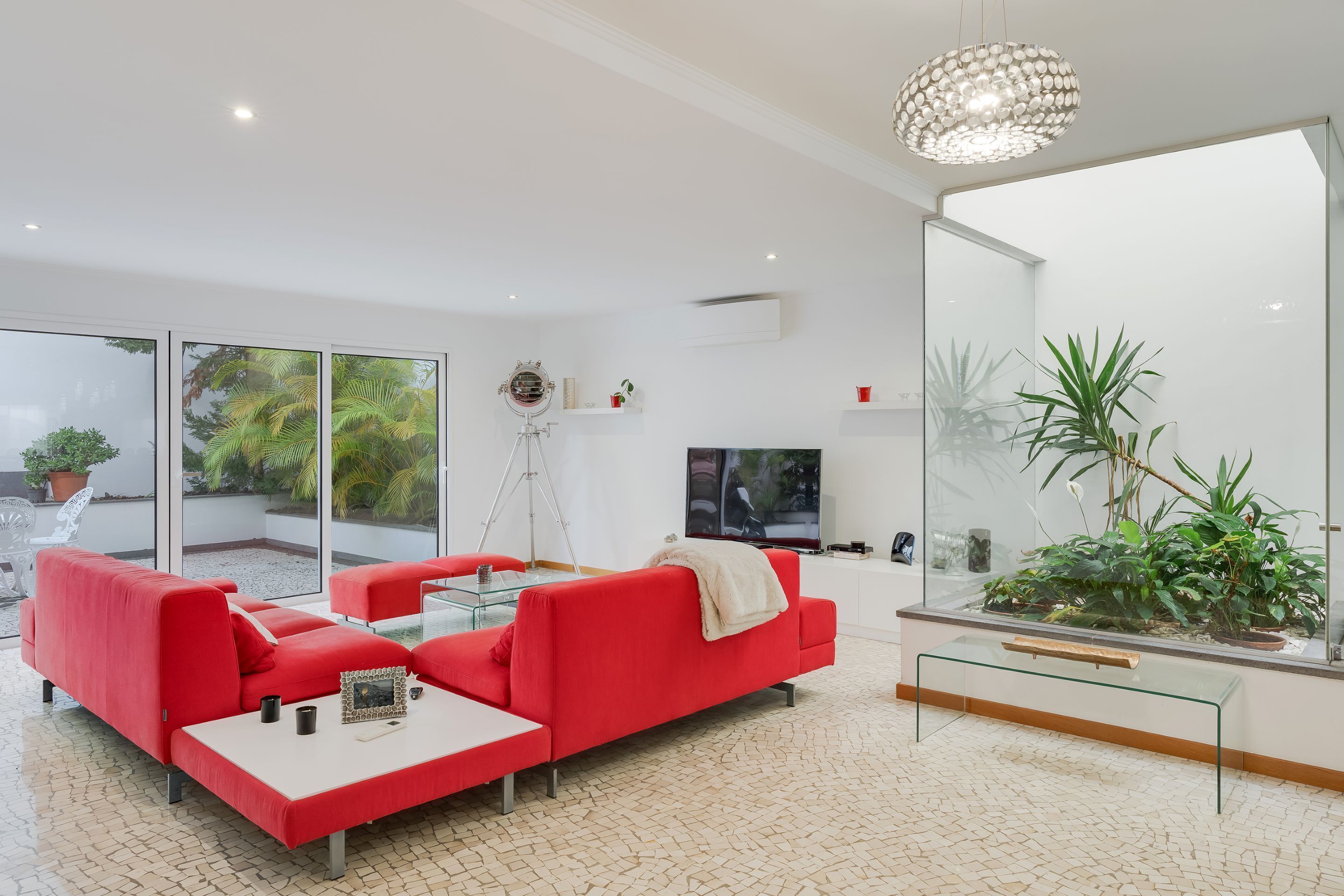 A modern living room with a red sofa set, a glass coffee table, and a large window offering a view of greenery outside.