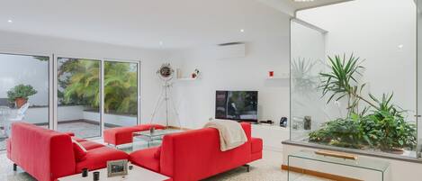 Un salon moderne avec un canapé rouge, une table basse en verre et une grande fenêtre donnant sur un paysage verdoyant.