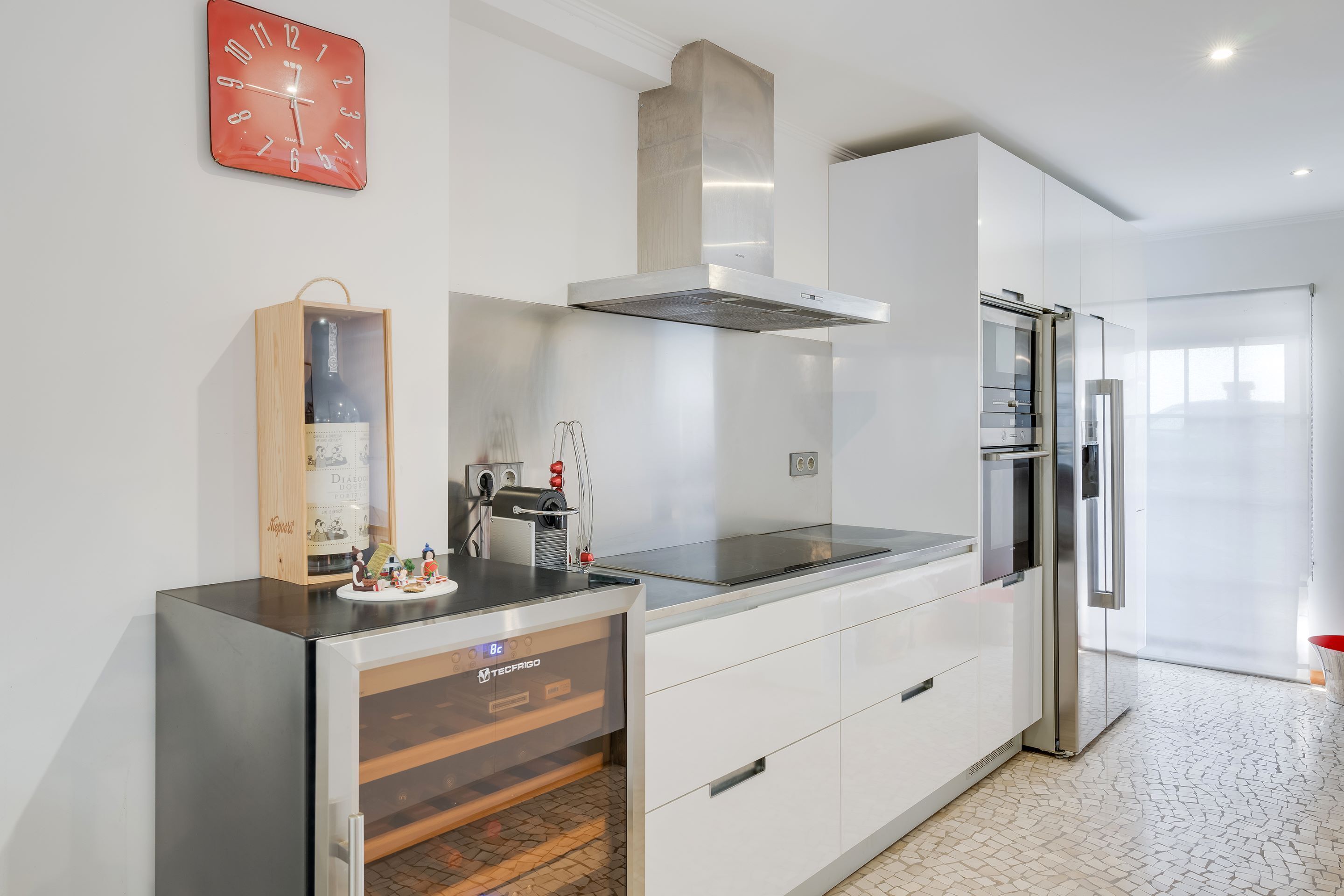A modern kitchen with a built-in oven, stainless steel appliances, and a wooden cabinet with a wine bottle.