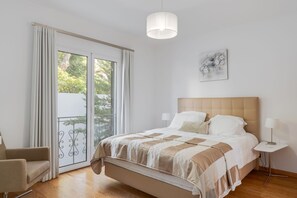 Ein Schlafzimmer mit Bett, Sessel, Nachttisch, Lampe und Blick durch eine Schiebetür.