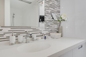 Ein modernes Badezimmer mit einem weißen Waschbecken, einem Spiegel und einer gefliesten Rückwand.