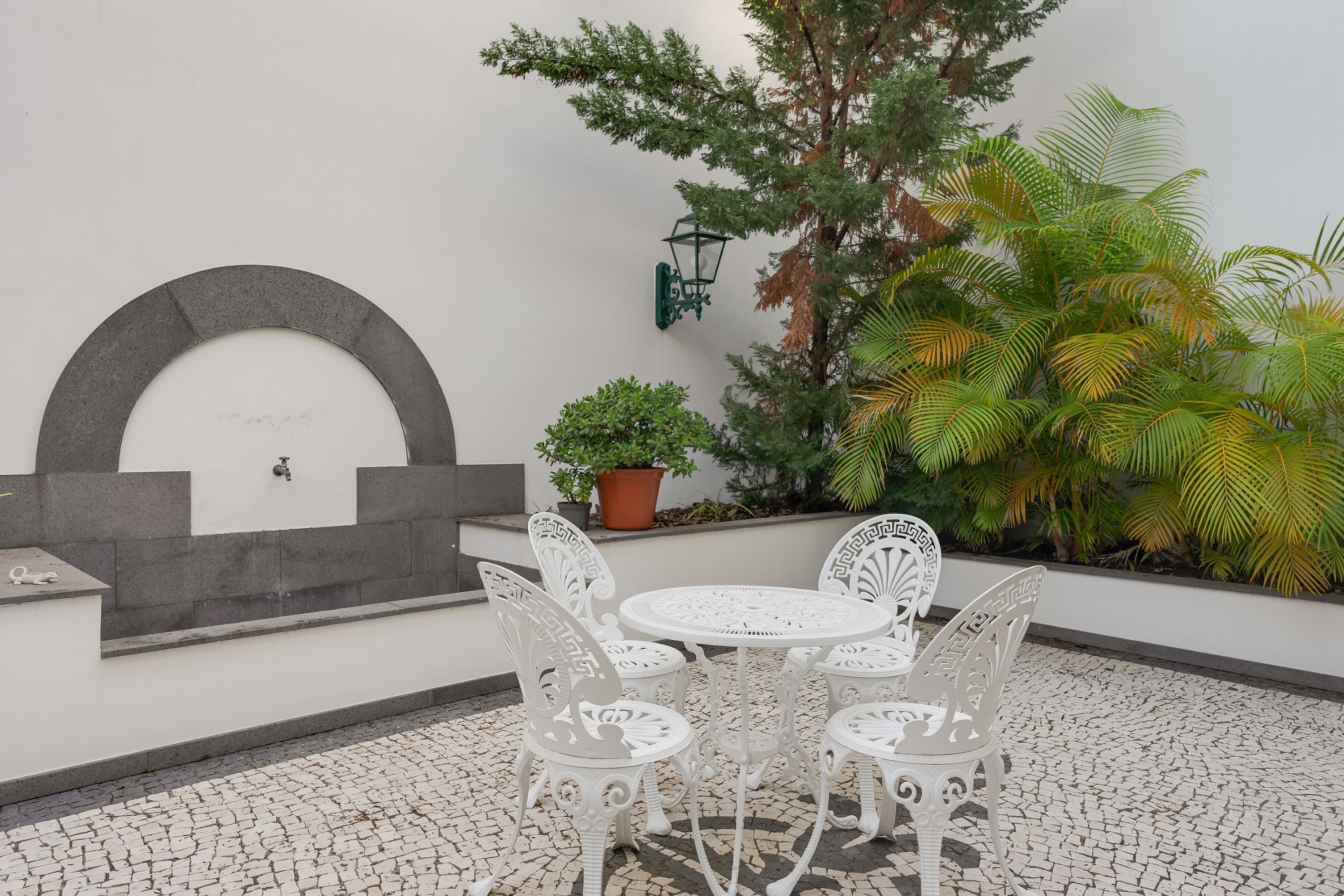 A patio with a white table and chairs, a decorative wall, and potted plants.
