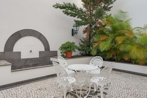 Eine Terrasse mit einem weißen Tisch und Stühlen, einer Zierwand und Topfpflanzen.