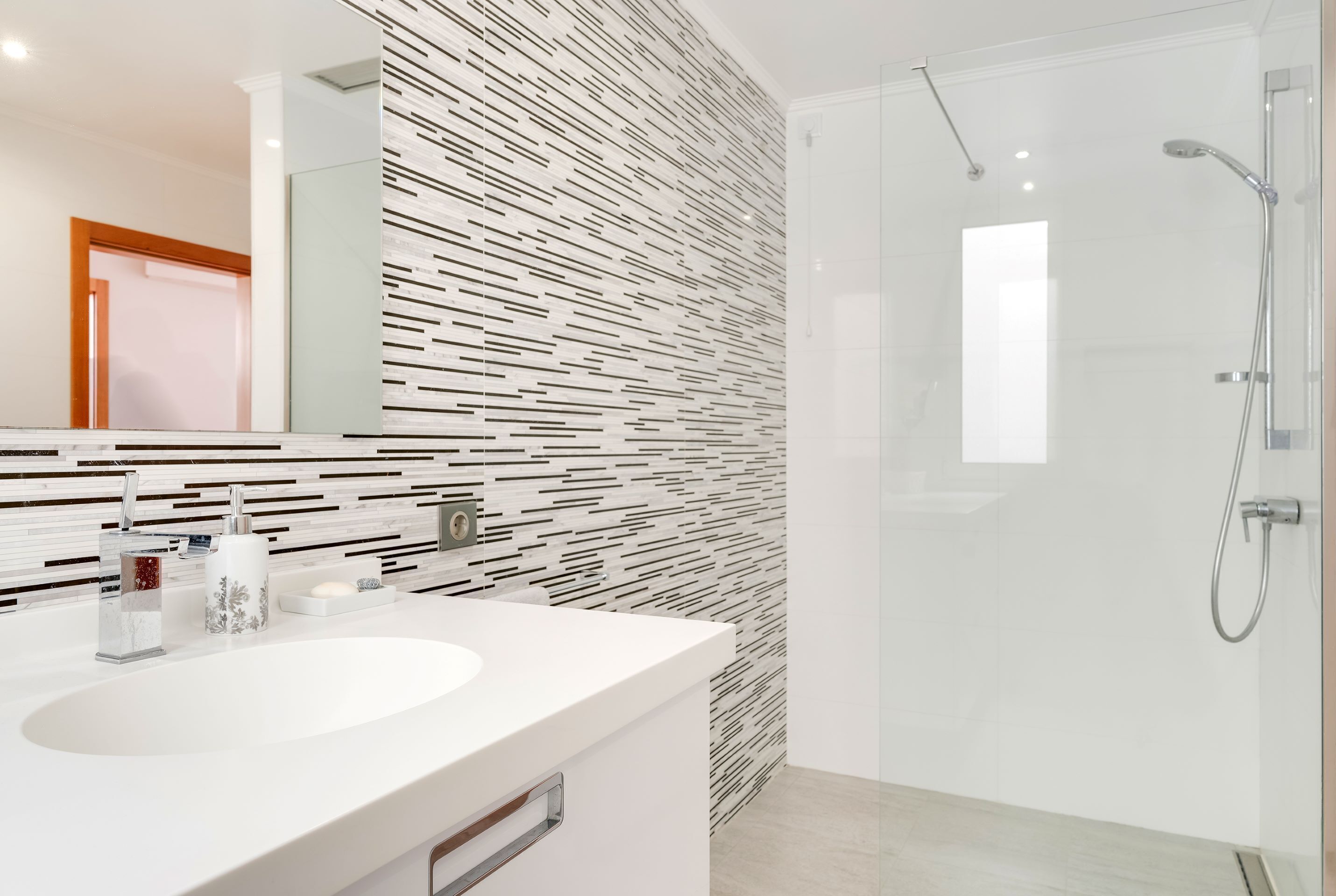 A modern bathroom with a white sink, a glass shower enclosure, and a patterned wall.