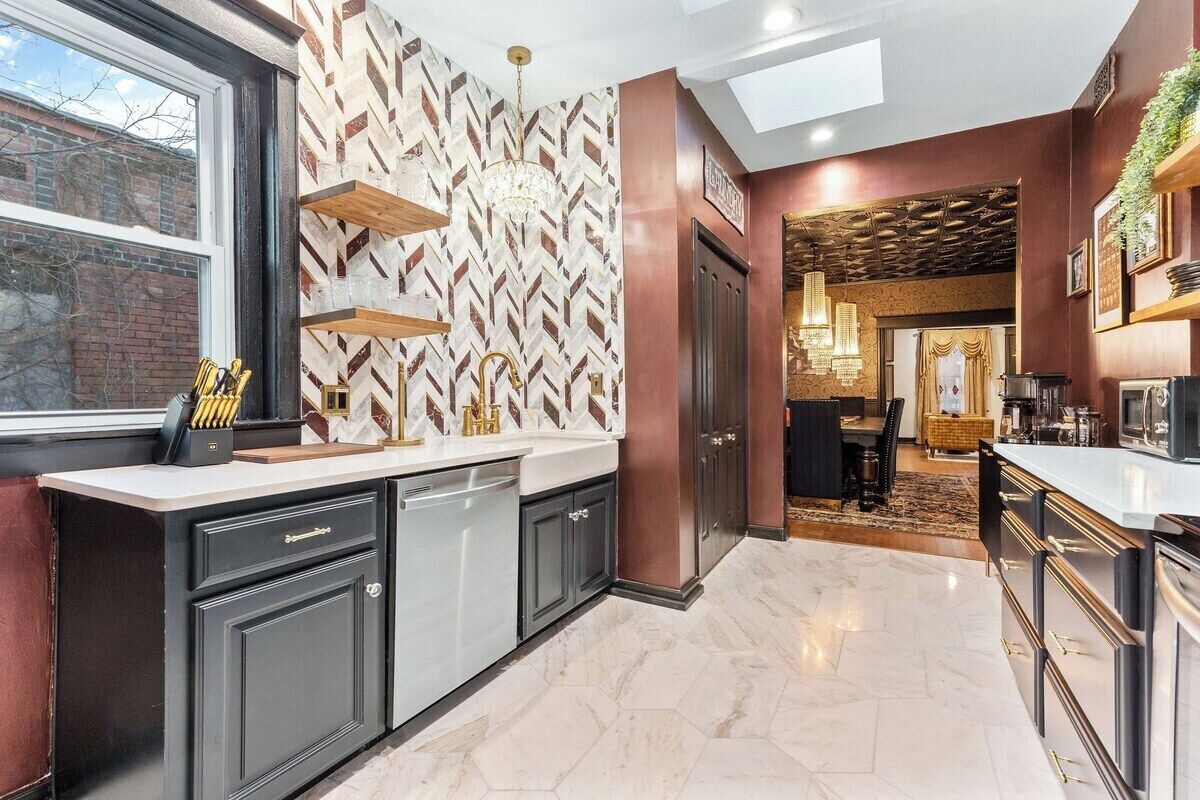 A modern kitchen with a herringbone-patterned backsplash, built-in appliances, and a large window.