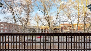 A view from a balcony with a metal railing, overlooking a parking lot and buildings with brick facades.