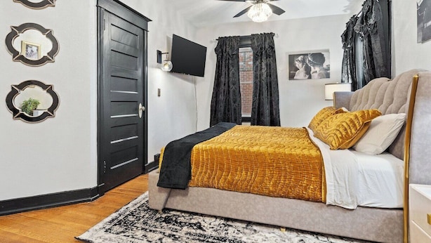 A bedroom with a bed, a ceiling fan, a TV, and a door.