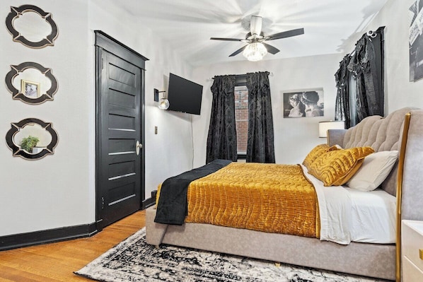 A bedroom with a bed, a ceiling fan, a TV, and a door.