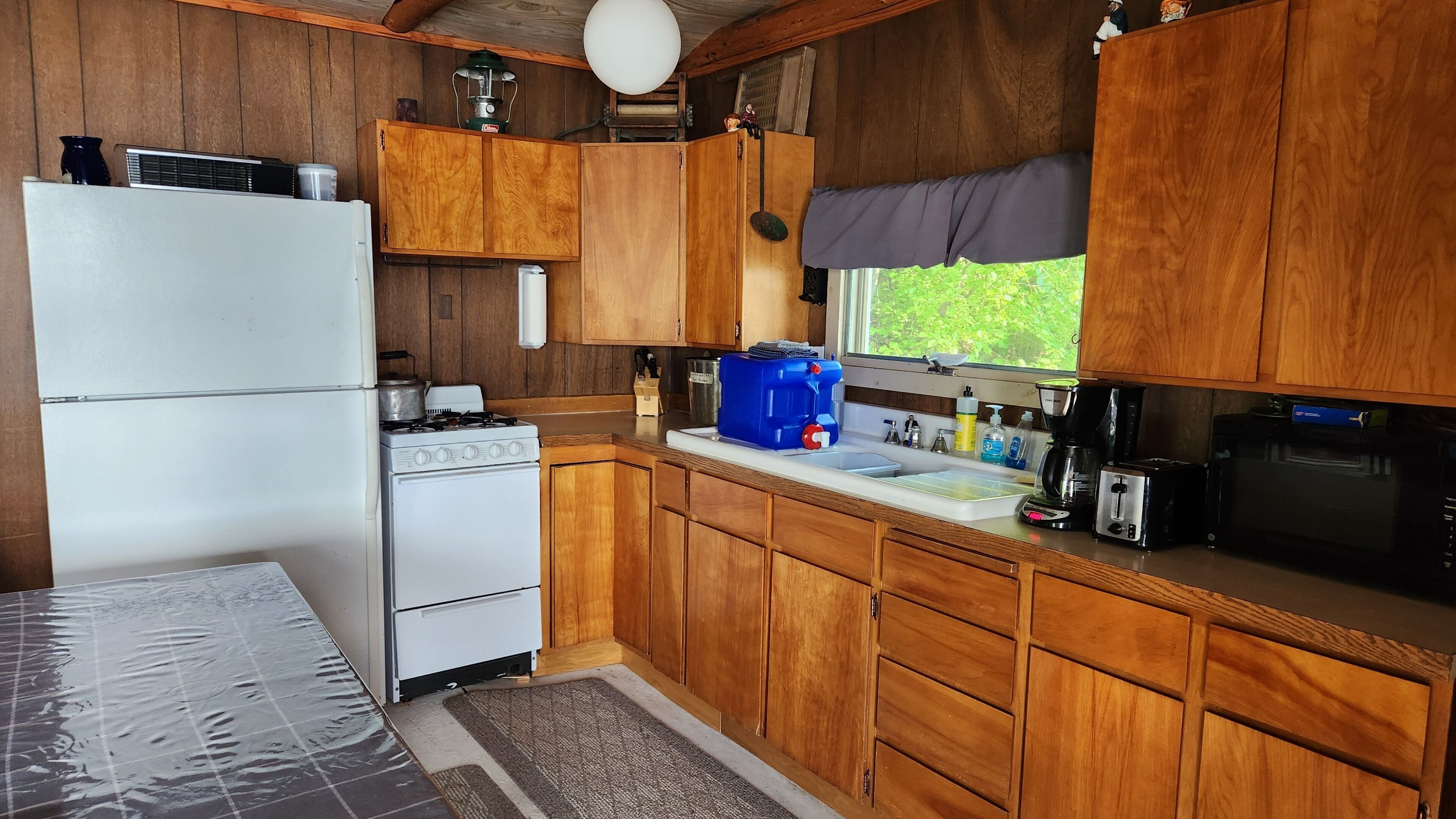 Une cuisine compacte avec des meubles en bois, un réfrigérateur blanc, une cuisinière, un distributeur d’eau bleu et un four à micro-ondes.
