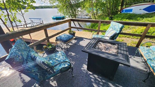 Una terraza con mobiliario exterior, un brasero y vista a un lago.