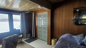 Una habitación con cama, una silla, un escritorio, una ventana con cortinas, una puerta y vistas a un paisaje nevado.