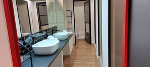 Een moderne badkamer met een lange wastafel, drie witte wasbakken en een grote spiegel.