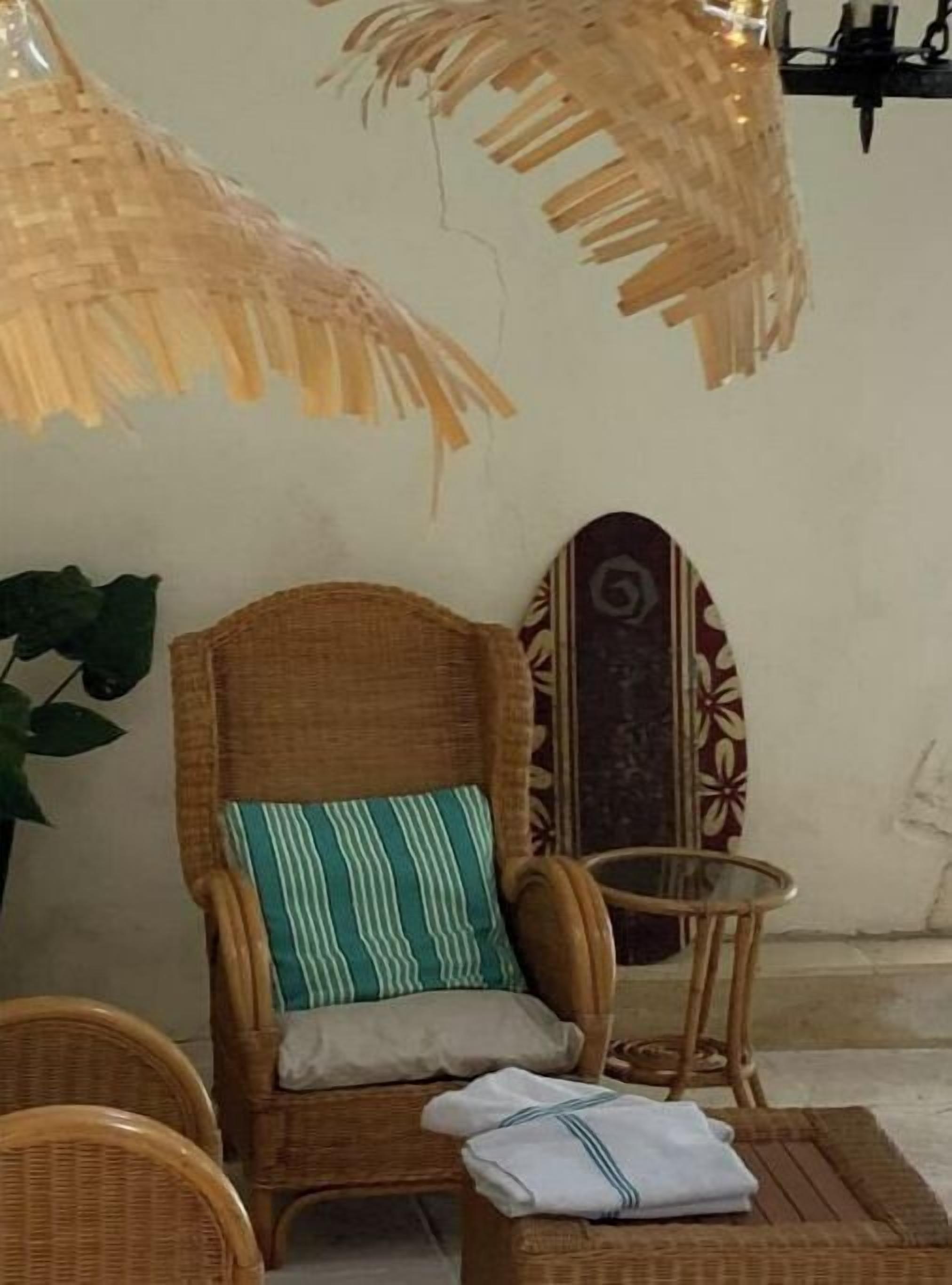 A wicker chair with a striped cushion, a small round table, and a folded towel on a woven mat.