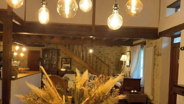 A dining area with a wooden table, hanging light bulbs, and a rustic decor. - The vacation home (Siorac-de-Ribérac)