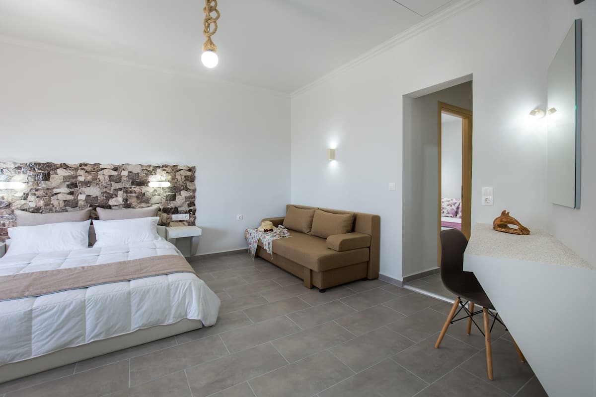 A modern bedroom with a large bed, a sofa, a desk, and a stone wall.